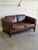 This two-seater sofa features plush brown leather cushions set within a structured rectilinear frame. Its low profile...