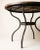 Round dining table featuring a substantial wood plank top paired with a curved wrought iron base. The tabletop has a warm,...