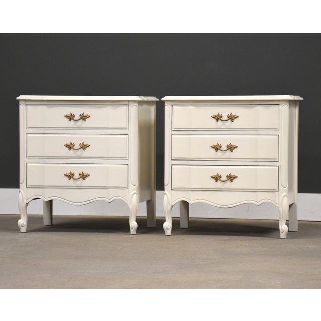A pair of French Provincial style chic white nightstands with patinated brass drawer pulls made by Dixie Furniture. 23.75”...