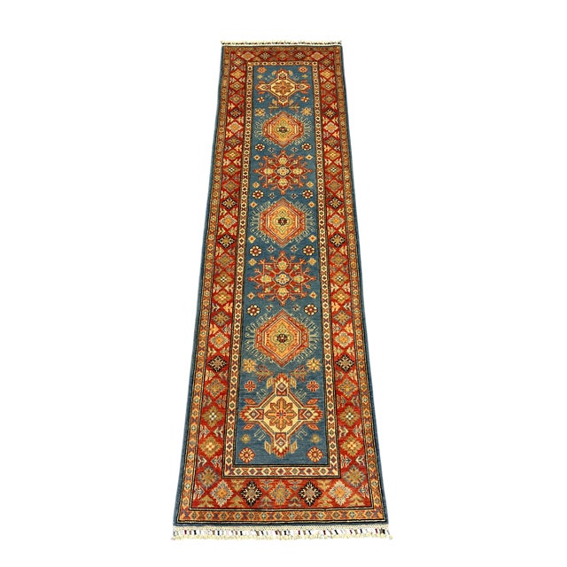 A natural dye wool runner with a blue field, rust red border, and accents of gold, cream, and green. Repeating Kazak-style...