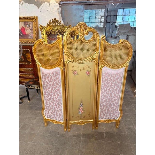 A striking French Louis XV-style boudoir ensemble combining an ornate gilt armchair with a dramatic three-panel decorative...