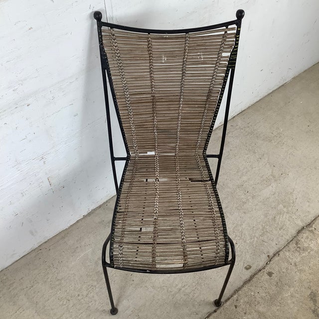 This vintage dining chair pairs a sculptural wrought iron frame with a handwoven reed seat and back, creating a striking...