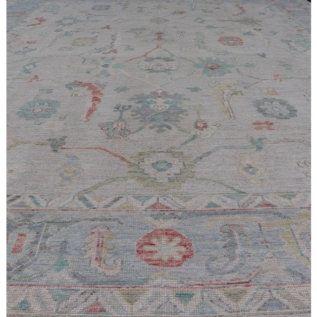 Large Modern Oushak with floral design on light blue/gray border with pops of color. Keivan Woven Arts; rug AWR-9004...