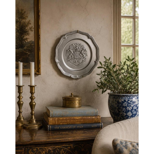 A handsome mid-20th-century German pewter wall plate centered by an elaborate heraldic coat of arms. The relief decoration...