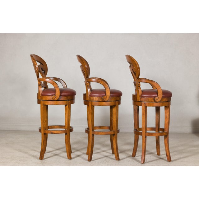 A set of three wooden swivel bar stools with carved backs. Elevate your home bar or kitchen island with this exceptional...