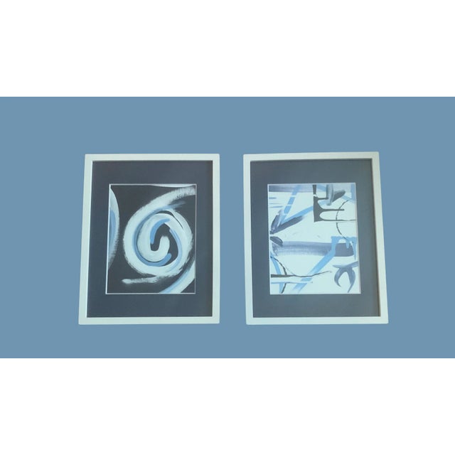 A pair of modern abstract paintings. In white frames with navy blue mats. Paintings are 8X10. Created by artists Kate Sansom.