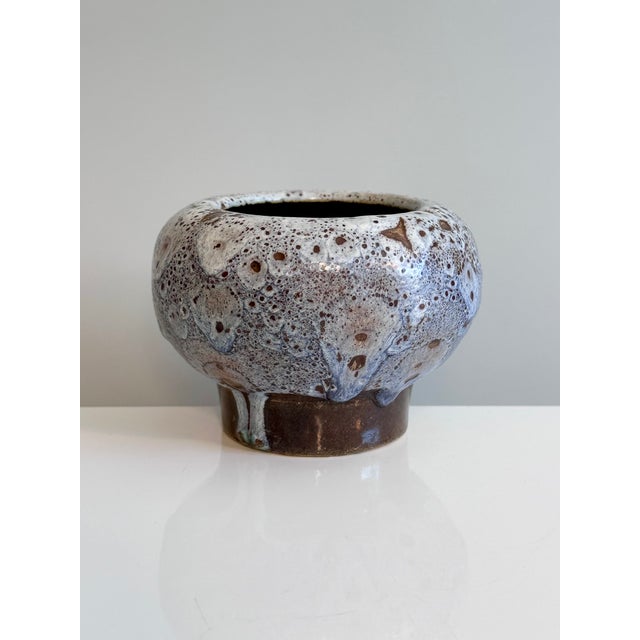 This hand-thrown ceramic vessel with a thick lava glaze in shades of blue on a brown background was crafted in the...