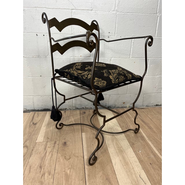 A striking vintage wrought iron armchair featuring a sculptural curule-style base, gracefully scrolled arms and feet, and...
