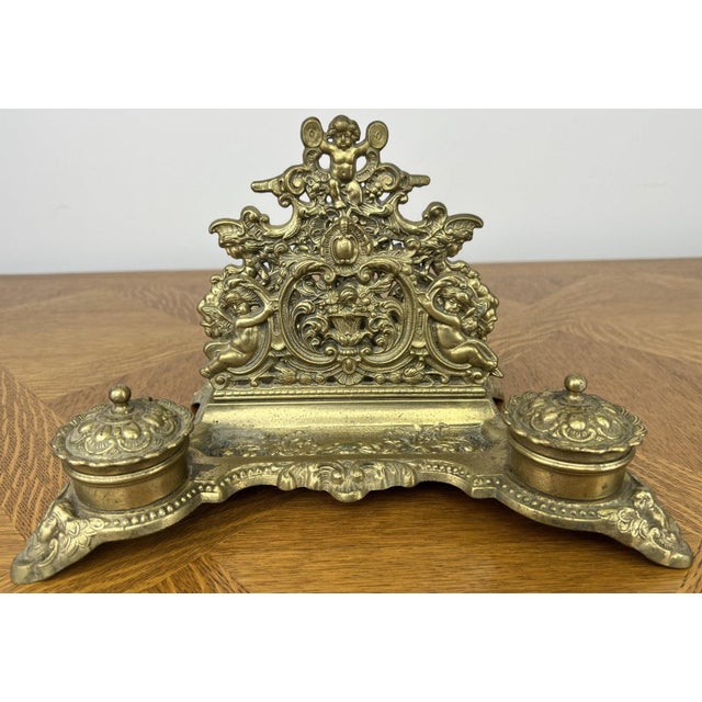 An exceptionally decorative Vintage brass inkwell set featuring ornate cherub detailing and elegant classical styling...