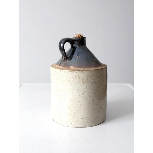 This antique stoneware crock jug features a brown slip top and a natural tone glazed base. Holding about two gallons, it...