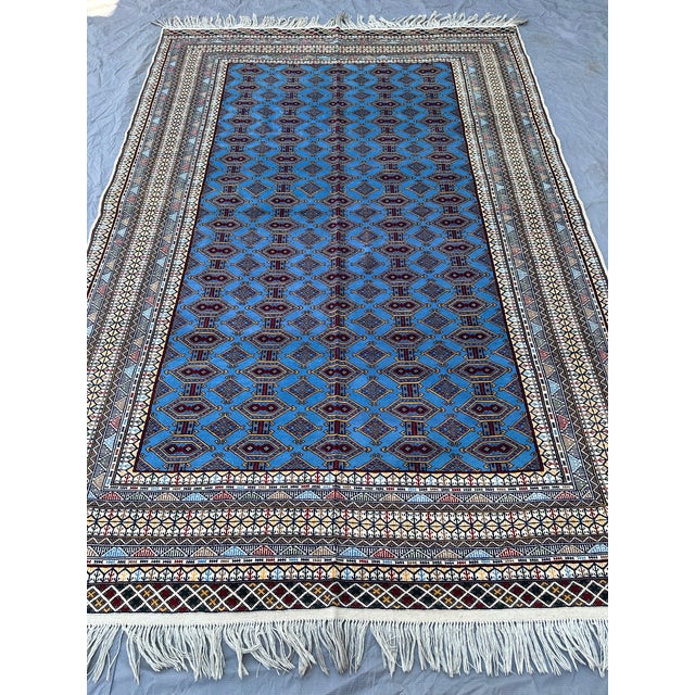 This striking Turkmen Bokhara rug presents the classic repeating "gul" medallion lattice in a rich sky-blue field, a...