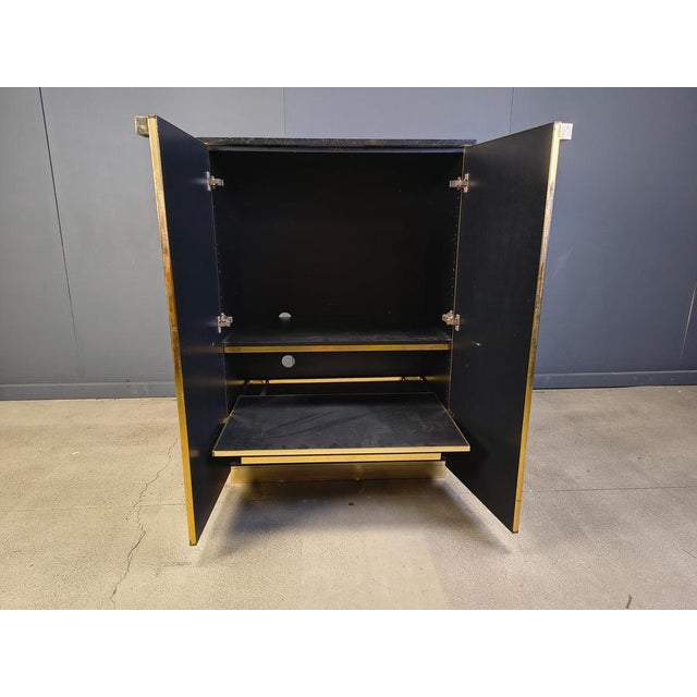 Hollywood regency black lacquer and brass bar cabinet with a black marble top. The cabinet offers plenty of storage space...