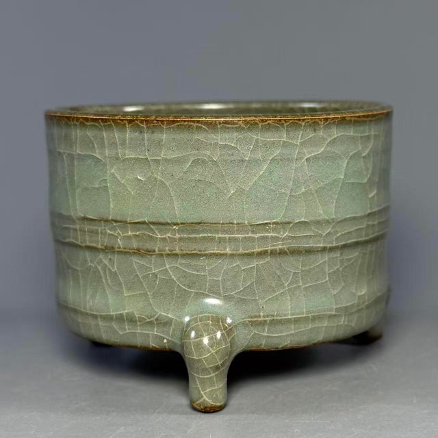 A stately Chinese celadon tripod vessel, showcasing restrained oriental beauty. The cylindrical body is adorned with...
