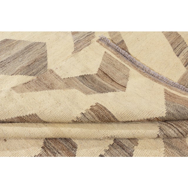 A hand-knotted Kilim rug with a geometric design on a beige field. Accents of brown and beige throughout the piece. This...