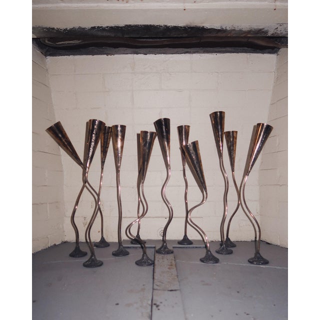 A collection of twelve vintage sculptural metal candlesticks featuring elongated adjustable stems, tapered cone tops, and...