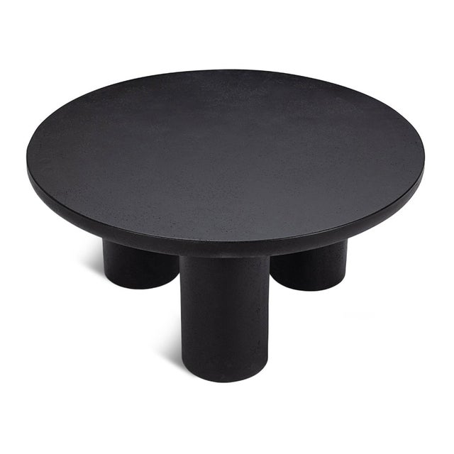 Modern round coffee table crafted from black finish fiber-reinforced concrete with a sculptural three-pillar base. The...