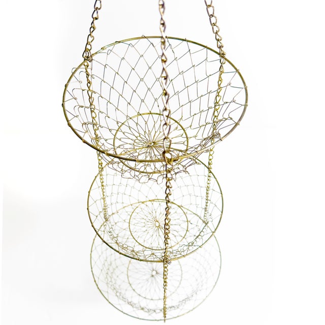 Vintage brass-tone metal hanging fruit basket with three graduated wire bowl tiers and a hook at the top for easy hanging....