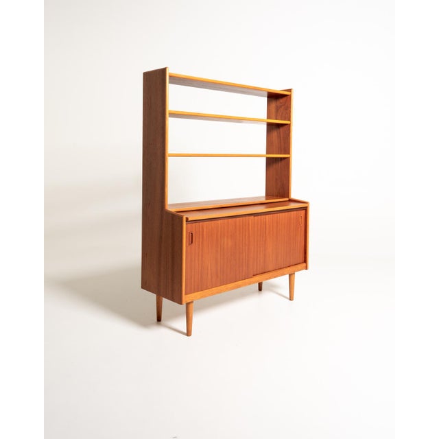 Teak bookcase with open shelves, a pull-out desk, and a lower compartment with sliding doors and an internal shelf....