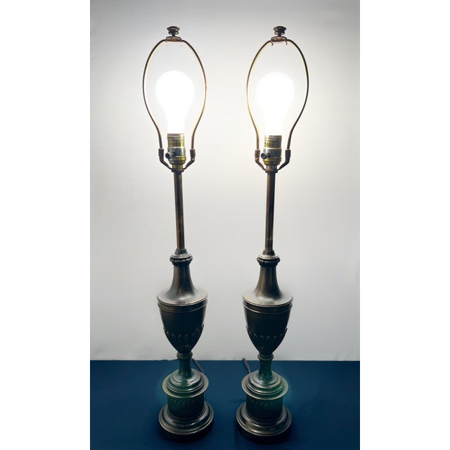A commanding pair of heavy cast metal lamps showcasing a refined Neoclassical silhouette. The urn-form bodies feature deep...