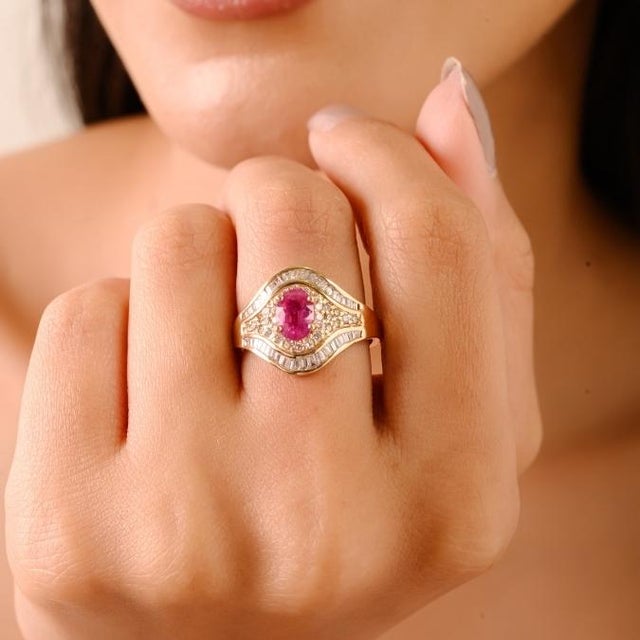 This elegant ring showcases an oval-cut ruby weighing 1 carat, surrounded by brilliant round and baguette-cut diamonds...