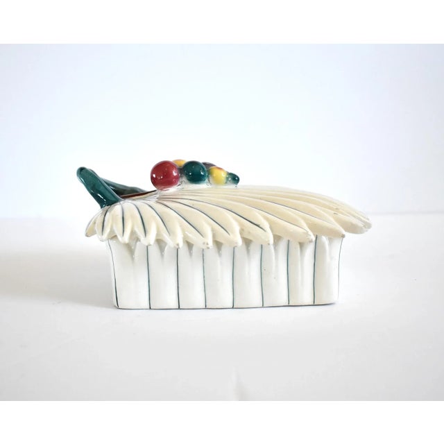 A vintage ceramic tin-glazed trinket box with side and lid of white and green palm frond leaves, with colorful palm...
