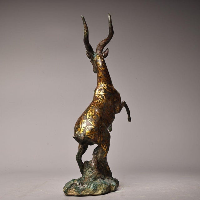 This decorative bronze sculpture depicts a dynamically posed antelope / goat with front legs raised. The body is adorned...
