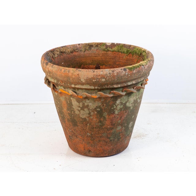 A large antique terracotta pot featuring a wide flared rim and a decorative rope twist detail encircling the upper body....
