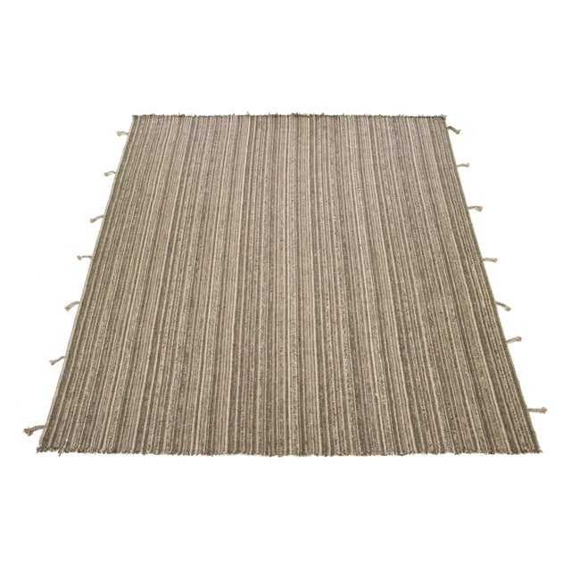 A contemporary flatweave kilim rug features a beige, tan, and brown color field with an all-over geometric design and...