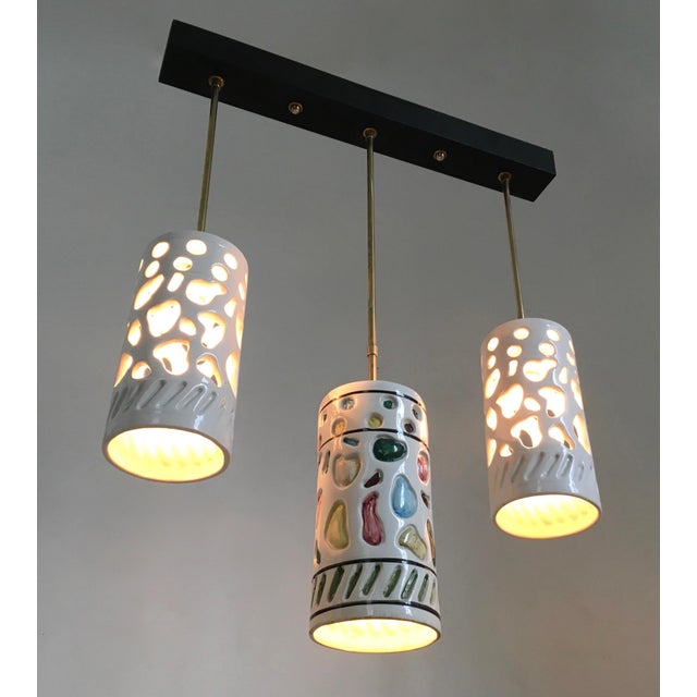 Made in Italy, 1960s. This chandelier features three white cylindrical ceramic lampshades with colored details and a...