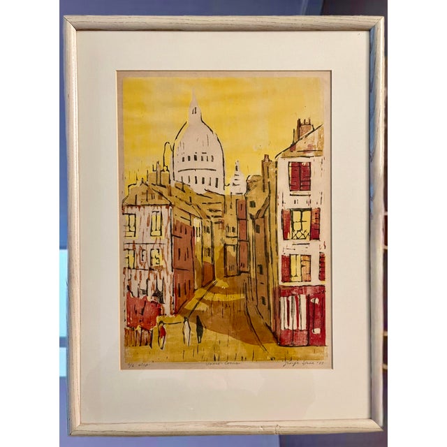 A colorful, expressive signed print of Sacre Coeur by George Speck. Encased in a bleached wood frame with white matting.