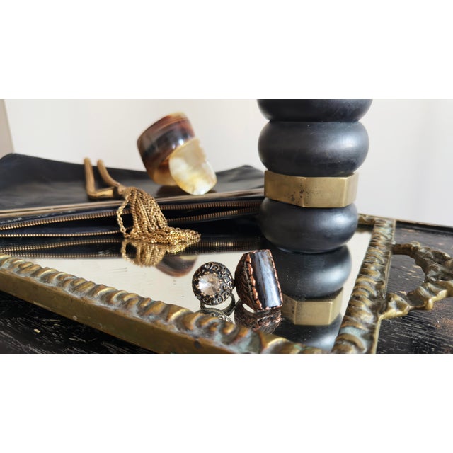 Brutalist cocktail ring featuring a raw black onyx held by jagged prongs in a sculptural metal band. Filigree detailing...