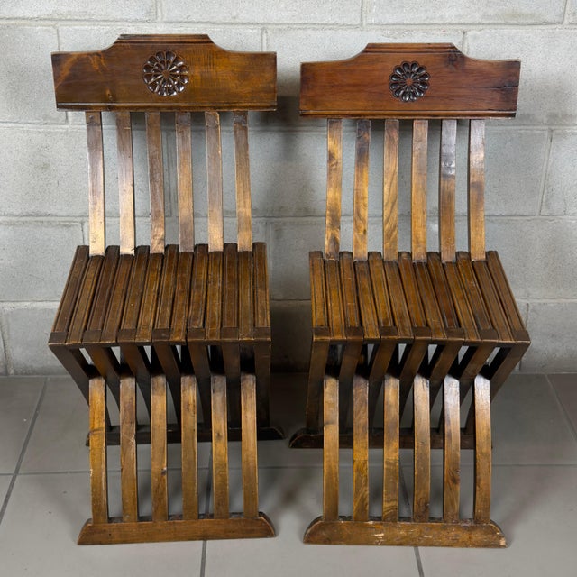 A pair of Savonarola-style folding chairs attributed to 20th-century Italian craftsmanship, made of solid wood with a...
