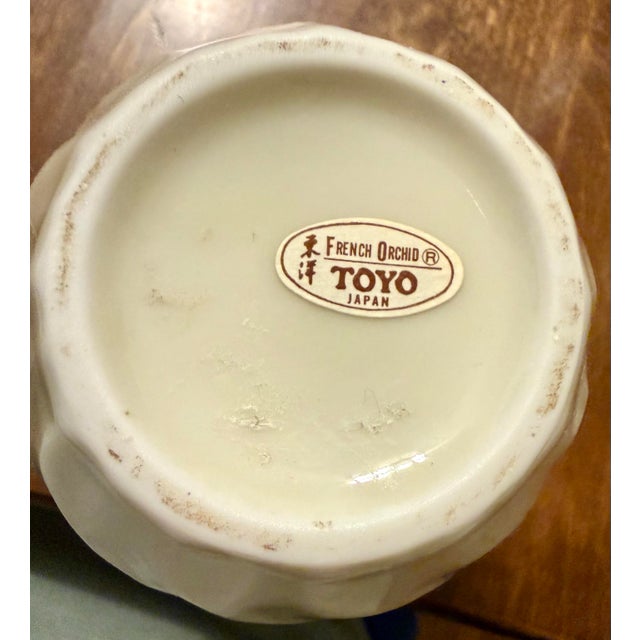 The taller vase is made by ‘Fine China of Japan’ a brand known for producing decorative ceramic items. It is an eye...