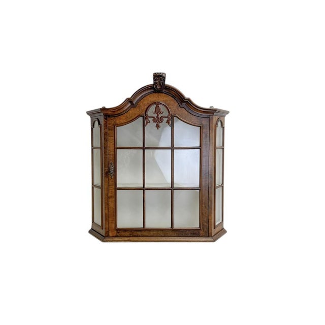 A charming mid-century walnut veneer display cabinet with a glass door and white scalloped shelves inside. The cabinet...