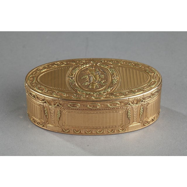Three-tones gold oval snuff box. The hinged lid is decorated with a country trophy medallion. The medallion is framed by a...