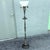 Elegant antique floor lamp featuring a tall, slender weighted metal body with ornate Neoclassical detailing throughout....
