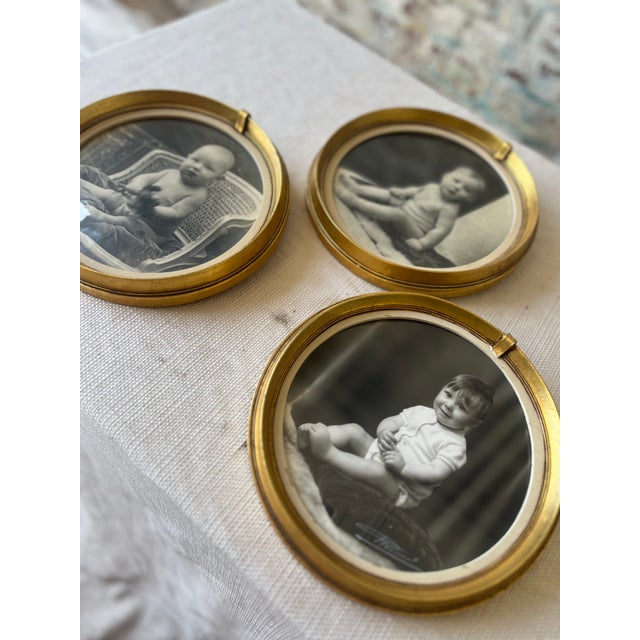 A charming trio of vintage round gold frames, each encasing a timeless black-and-white baby portrait [these can be...