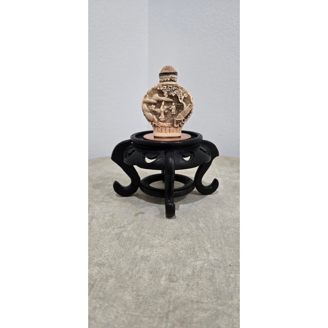 This hand-carved Chinese snuff bottle features a raised scenic landscape with figures in a garden setting and comes...