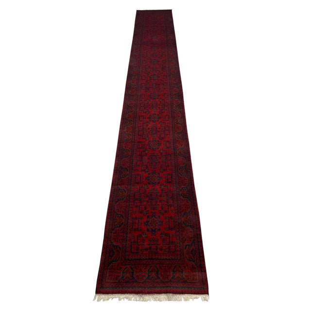 This extra-long wool runner features a deep red field filled with repeating geometric medallions in navy and warm rust...