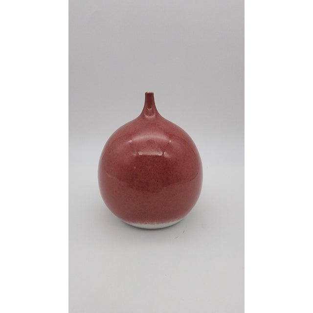 Elegant hand-thrown ceramic bottle vase with a softly rounded globe form and slender neck. Finished in a rich cranberry-...