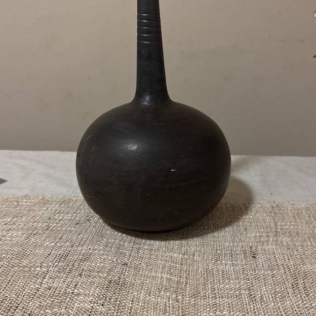 This striking ceramic vessel features a beautifully rounded, wide base that tapers into a tall, slender neck—creating an...