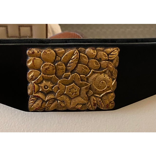 A striking black lacqured wood wall mirror with 3 geometric gilded floral appliques. The geometric beveled mirror has 7...