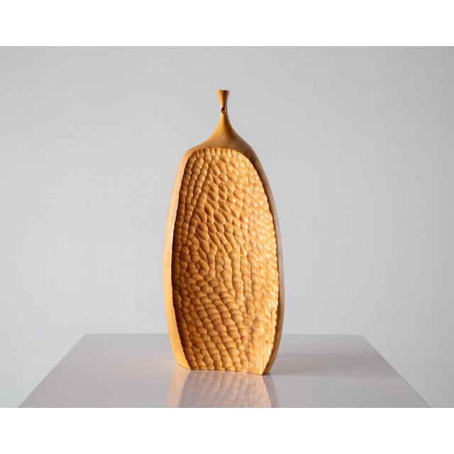 An organic form with chip carved accents, topped with a thin corseted neck and spout. This piece executed in camphor wood...