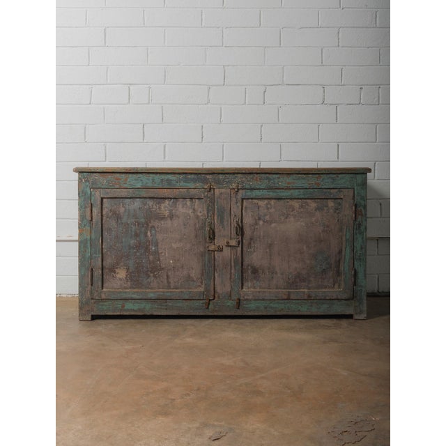 An evocative wooden sideboard shaped by decades of use, where layers of turquoise paint soften into muted clay and mineral...