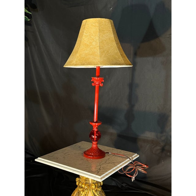 Decorative table lamp featuring a glossy deep red base with an elegant vintage-style shape and a warm beige textured...