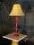 Decorative table lamp featuring a glossy deep red base with an elegant vintage-style shape and a warm beige textured...