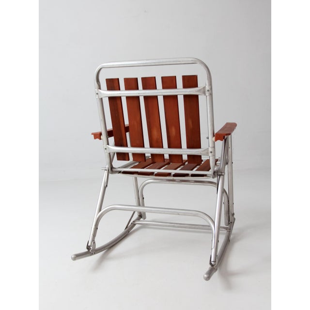 Vintage mid-century folding rocking chair combining a lightweight aluminum frame with warm wood slats for a timeless...