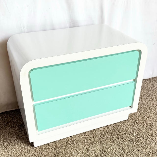 This striking postmodern nightstand features a sculptural waterfall silhouette finished in crisp white laminate, accented...