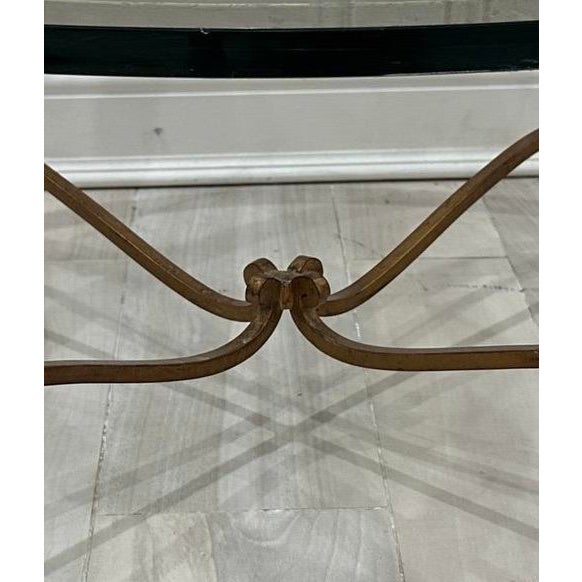 A vintage Hollywood Regency style round coffee table with a thick beveled glass top, gilded iron base and cabriole legs...