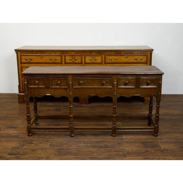 An English oak dresser base from the mid 19th century, with three drawers, scalloped apron and turned legs. Created in...
